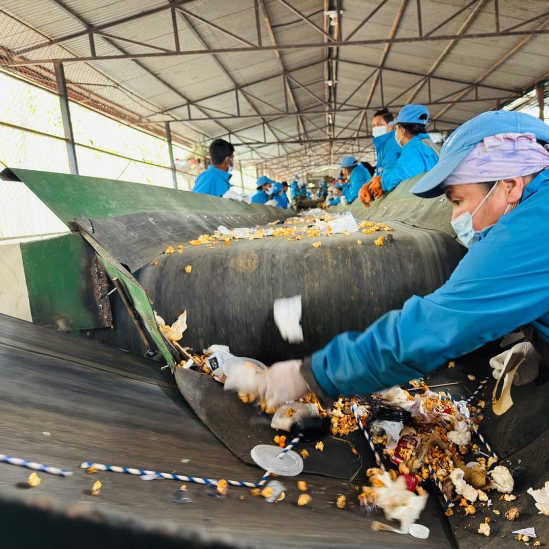 Equipe fazendo a triagem de materiais recicláveis em esteira, dentro de uma central de resíduos.