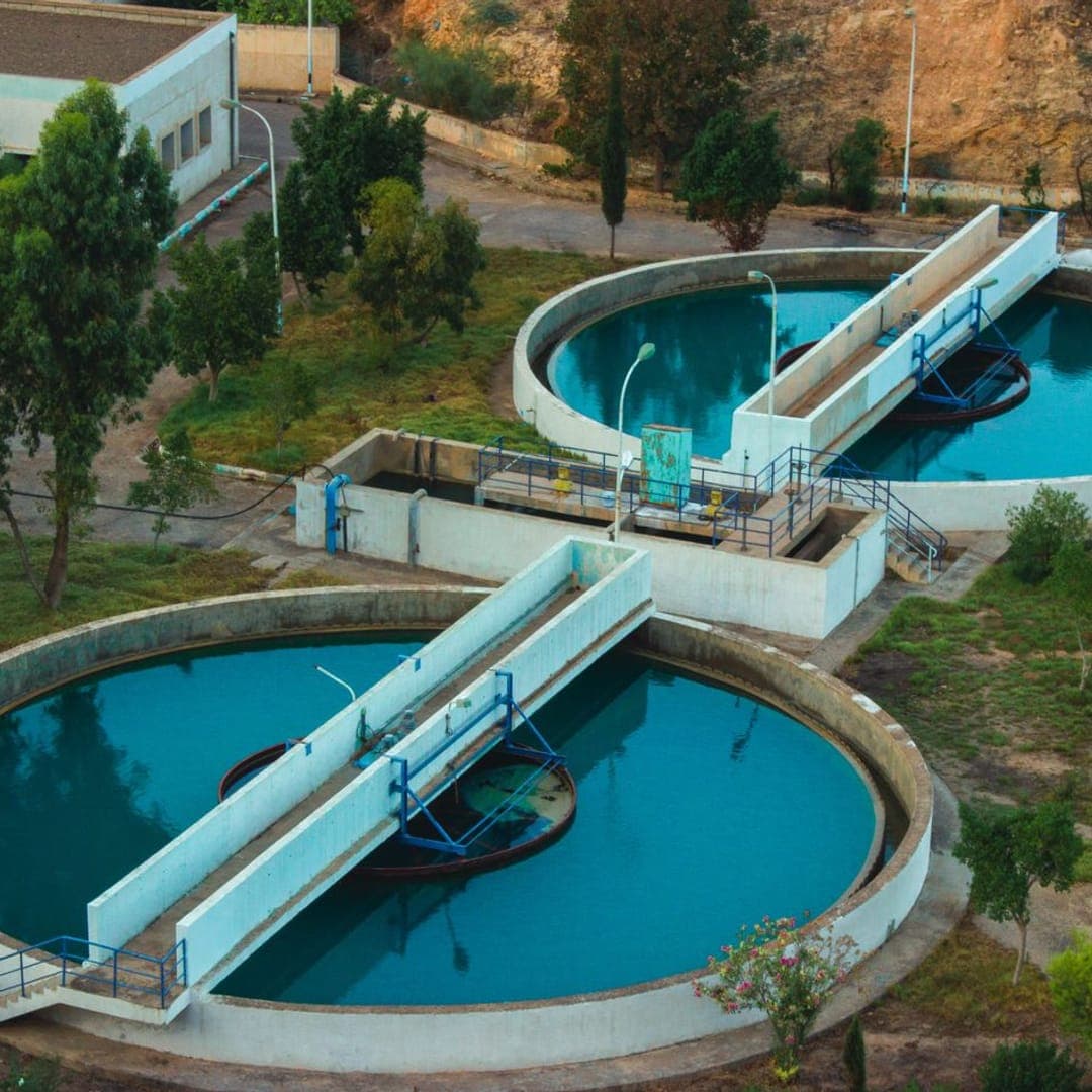 Estação de tratamento com tanques circulares de decantação, cercada de vegetação.